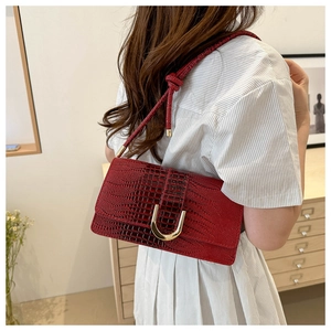 Detail of red crocodile texture handbag featuring a gold U-shaped buckle and knotted strap