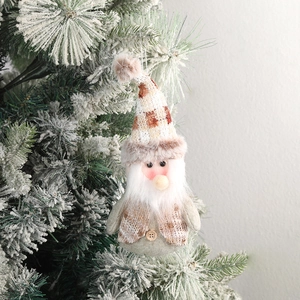 Plush Christmas gnome ornament with knitted hat and faux fur on a snowy tree branch