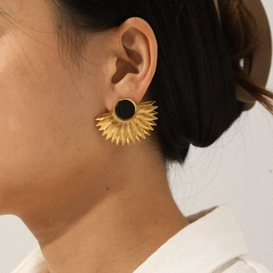 Close-up of a person wearing gold fan-shaped sunburst earrings with a black round center