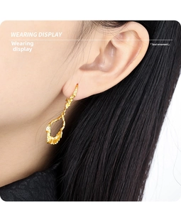 Close-up of irregular hollow lava texture drop earrings in gold plating on model