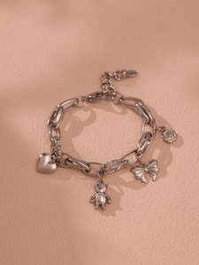 Detail of silver stainless steel chain bracelet with heart, bear, and bow charms