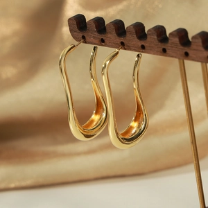 Elegant gold-tone irregular U-shaped geometric metal earrings on a wooden stand