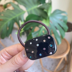 Detail of a black rectangular hair tie with colorful rhinestones and elastic band