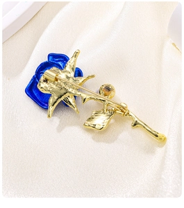 Close-up of elegant blue enamel rose brooch with gold leaves on beige silk fabric
