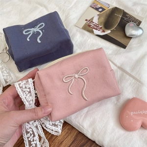 Detail of bow-embroidered canvas cosmetic bags in pink and blue with lace ribbon accents
