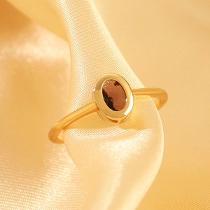 Detail shot of a gold oval brown zircon ring resting on smooth warm silk fabric