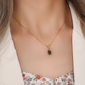 Close-up of a gold chain necklace with a black rectangular pendant on a fashion model