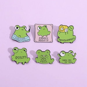 Collection of six green enamel frog pins with humorous captions on a purple background