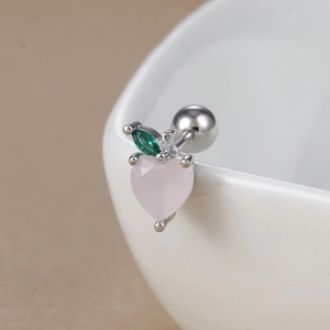 Macro shot of pink heart-shaped peach stud earring with green zircon leaves on ceramic cup