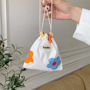 Floral fabric drawstring bag with orange and blue flowers held by hand in home setting