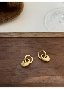 Nahaufnahme goldener ovaler Ohrringe mit matter Textur auf einem Holztablett