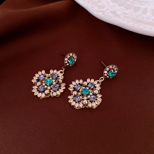 Detail view of vintage diamond-shaped earrings with blue gems on dark velvet