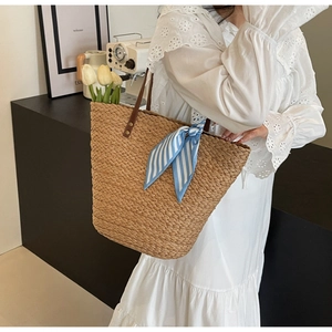 Detail of straw woven tote bag featuring a blue striped scarf and leather handles