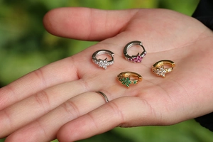 Detail of four mini star drop hoop earrings with colorful zircon stones held in palm