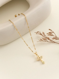 Detail of a gold cross pendant necklace on ripple chain with refined metallic shine