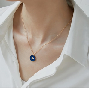 Close-up of golden compass pendant with blue enamel on a model wearing white shirt