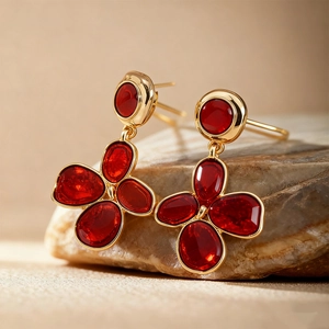Close-up of golden floral earrings with red oval gemstones on a natural stone base