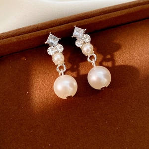 Detail of luxury pearl earrings with square and round rhinestones on brown velvet