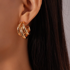 Close-up of a model wearing layered gold C-shaped hoop earrings with a glossy metal finish