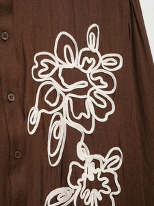 Close-up of brown textured shirt featuring white corded floral embroidery details