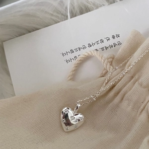 Close-up of a silver heart pendant with pavé zircons resting on a beige drawstring pouch