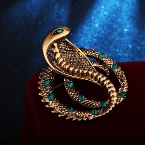 Detailed close-up of a vintage golden snake brooch featuring green rhinestones on red velvet