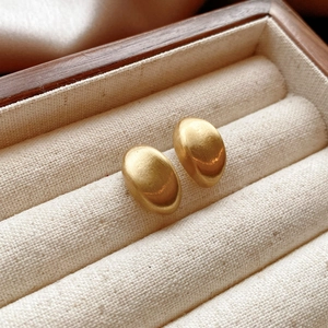 Detail of gold bean-shaped earrings with brushed metal texture in a wooden jewelry box