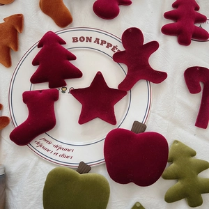 Flat lay of velvet Christmas ornaments in festive shapes like stars and trees on white fabric