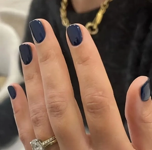 Macro shot of navy blue glossy artificial nails on hand with a chic gold necklace