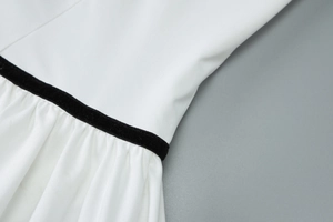 Détail de la robe blanche avec bordure en velours noir et texture de tissu plissé