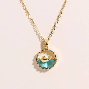 Elegant gold whale pendant necklace with blue crystal waves and a minimalist round frame
