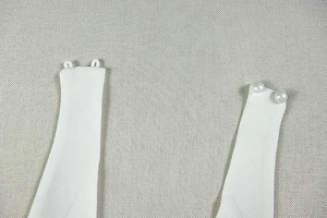 Detail of white dress shoulder strap featuring elegant pearl button and fine stitching