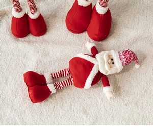 Close-up of red fabric plush Santa Claus doll with striped telescopic legs on white rug