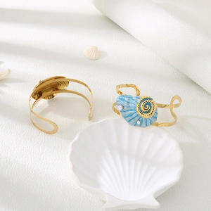 Detail of gold ocean style cuff bracelet with blue seashell charms and white pearls