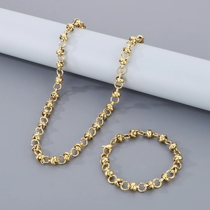Détail d'un ensemble collier et bracelet à maillons dorés sur fond gris neutre