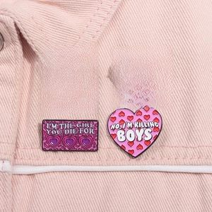 Détail de pins émaillés en forme de cœur rose avec slogans sur une veste en jean
