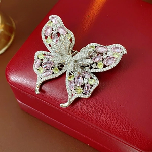 Close-up of butterfly brooch with pink and yellow zircons on a red leather jewelry box