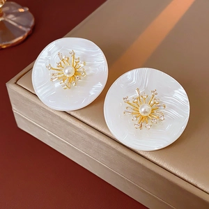 Detailansicht großer weißer Muschelohrringe mit Goldblumen und Perlenakzenten