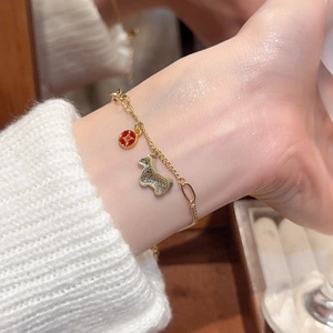 Detail of gold bracelet with a red round pendant and a sparkling zircon animal charm