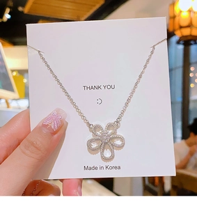 Close-up of a silver flower pendant necklace with clear cubic zirconia on a display card