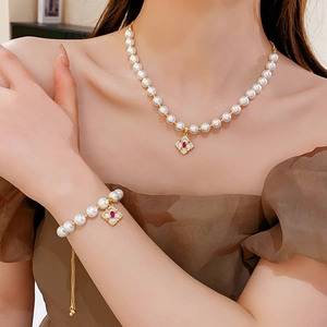 Detailed close-up of pearl necklace and bracelet with red flower pendant and gold beads