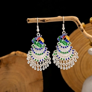 Close-up of Cloisonne peacock earrings with blue enamel details hanging on a branch