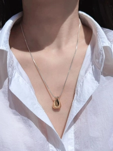 Close-up of gold water drop pendant on silver snake chain worn over a white linen shirt