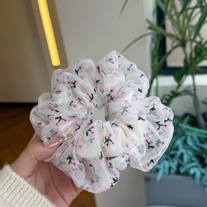 Gros plan d'un chouchou en maille blanche avec broderie florale rose et texture douce