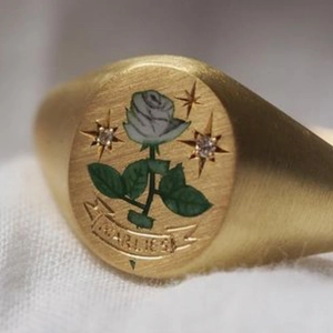 Macro shot of gold signet ring with hand-painted white rose and star engravings