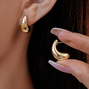 Detail view of gold teardrop earrings with a high-polish mirror finish on a model's ear