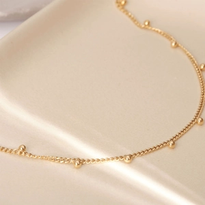 Close-up of 18K gold-plated stainless steel chain with small beads on a cream tray