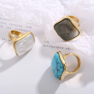 Detailed view of three gold-plated square rings with white, brown, and blue stone inlays