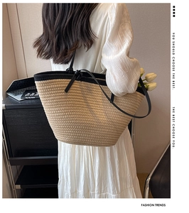 Large woven straw tote bag with black shoulder straps and knotted handle detail