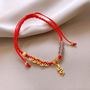 Dettaglio di un bracciale rosso intrecciato con ciondolo a serpente dorato e perle di agata